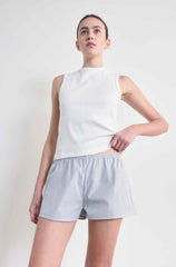 Woman wearing a white sleeveless top and striped shorts on a plain background