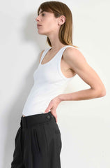 Woman wearing a white tank top and black pants against a plain background