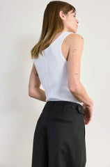 Woman wearing a white sleeveless top and black pants against a plain background