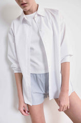 Person wearing a white oversized shirt and striped shorts on a plain background