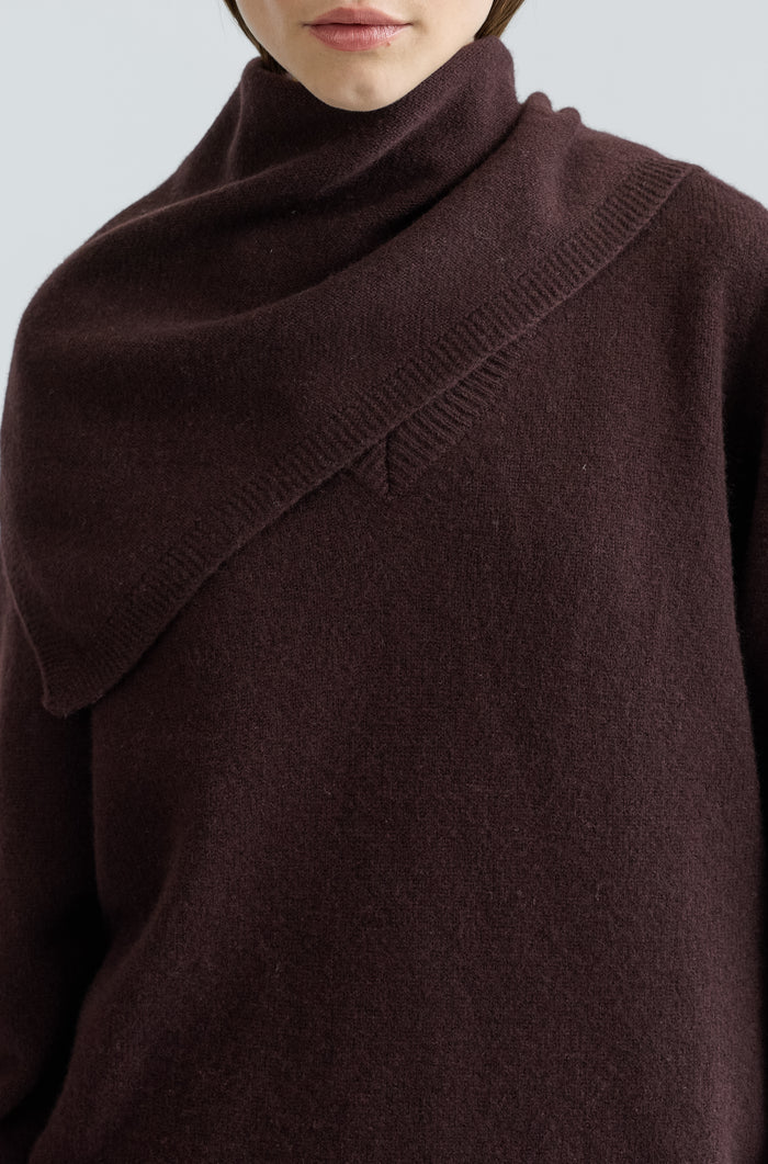 Woman wearing a dark brown scarf over a brown outfit on a light grey background