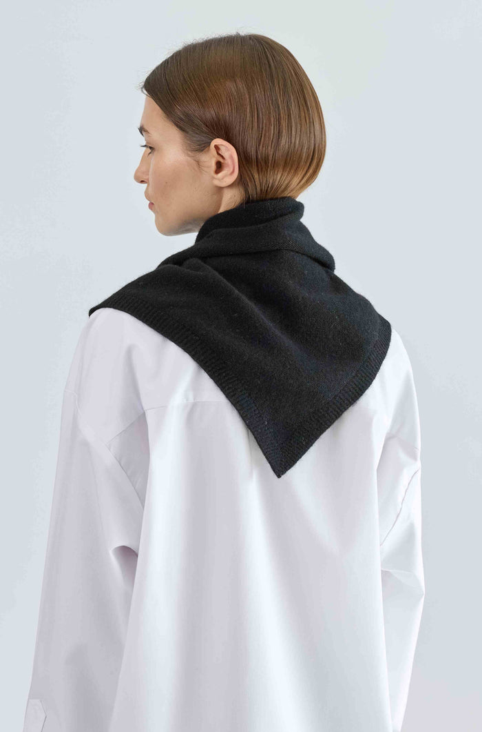 Person wearing a black scarf over a white shirt on a light gray background