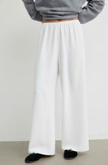 White wide-leg trousers worn by a model, paired with a gray long-sleeve top and black slip-on shoes, shown from the waist down against a plain light gray wall.
